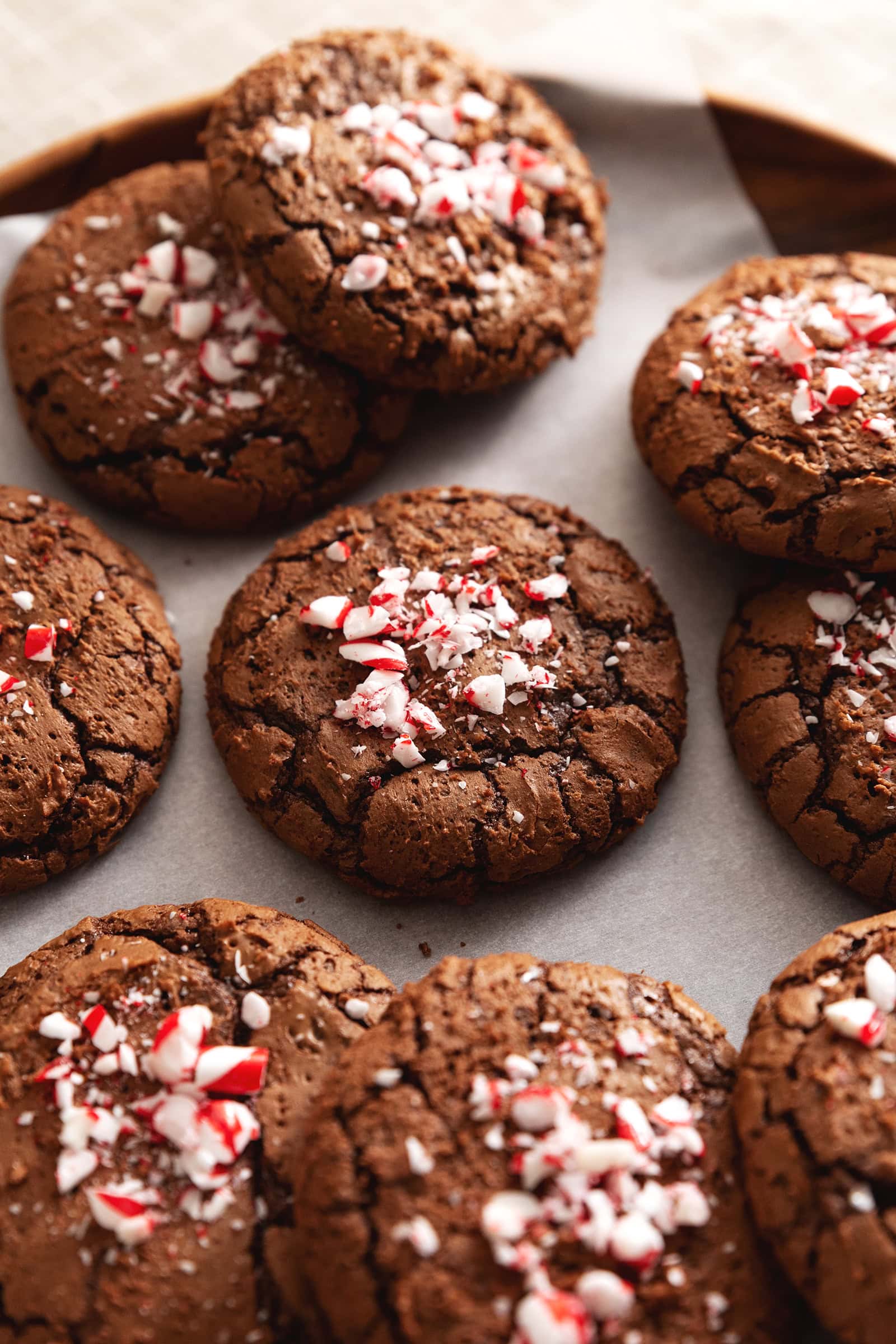Several chocolate peppermint cookies with crushed candy canes on top scattered on parchment paper.