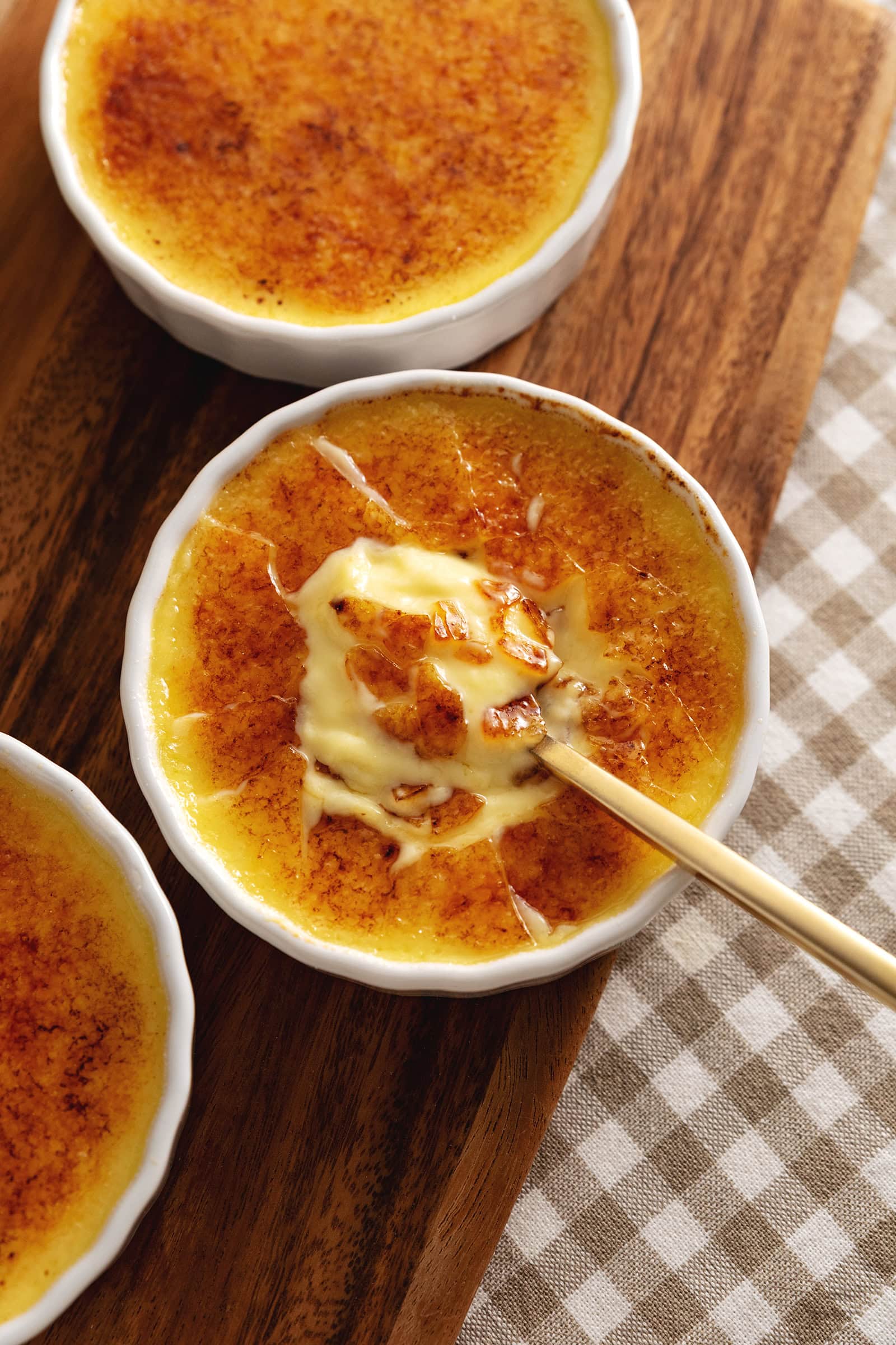 A ramekin of eggnog cr&egrave;me br&ucirc;l&eacute;e with a spoon resting in the custard under the crunchy sugar shards.