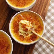 A ramekin of eggnog crème brûlée with a spoon resting in the custard under the crunchy sugar shards.