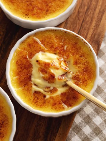 A ramekin of eggnog crème brûlée with a spoon resting in the custard under the crunchy sugar shards.