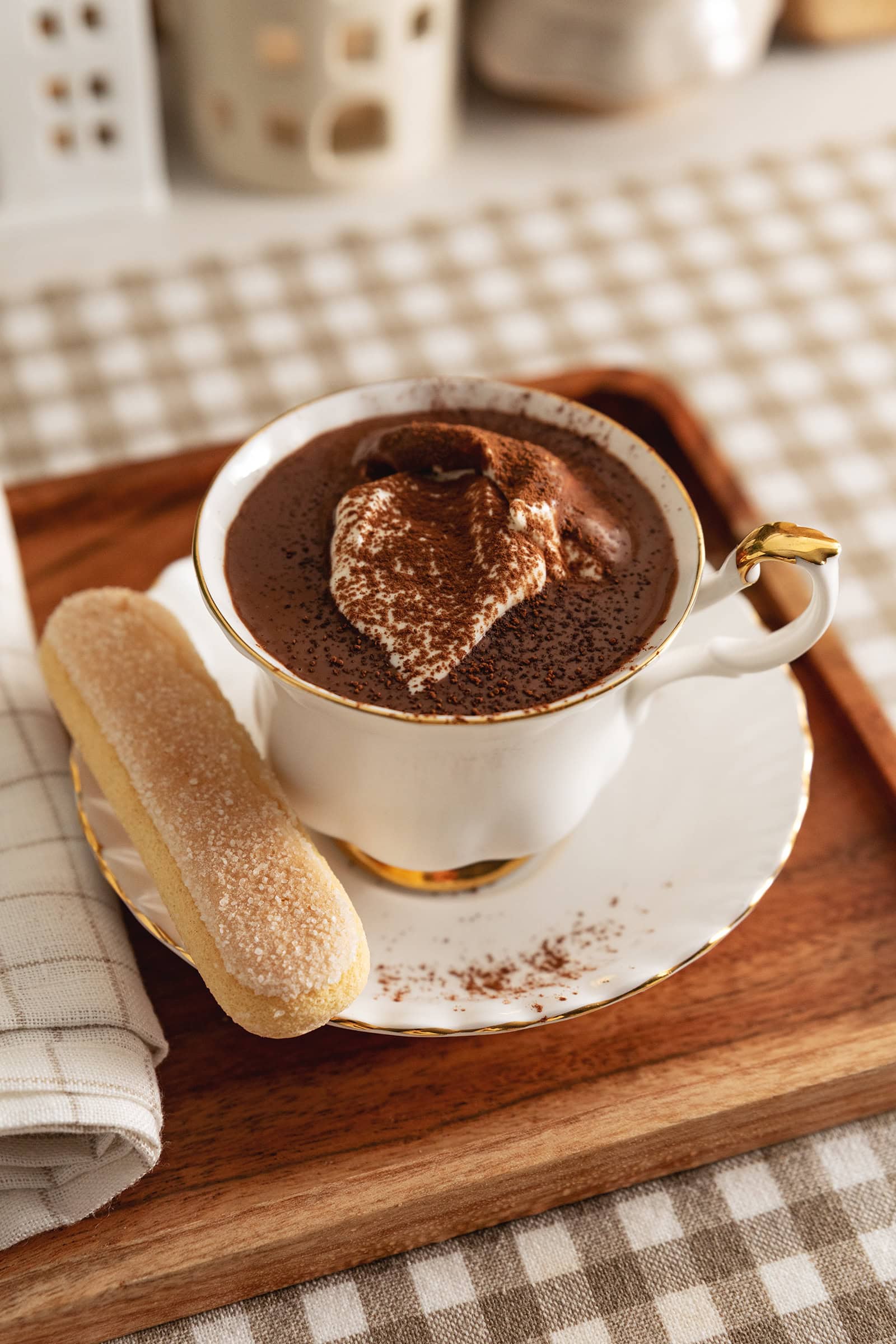 A teacup of tiramisu hot chocolate with a ladyfinger on the saucer.