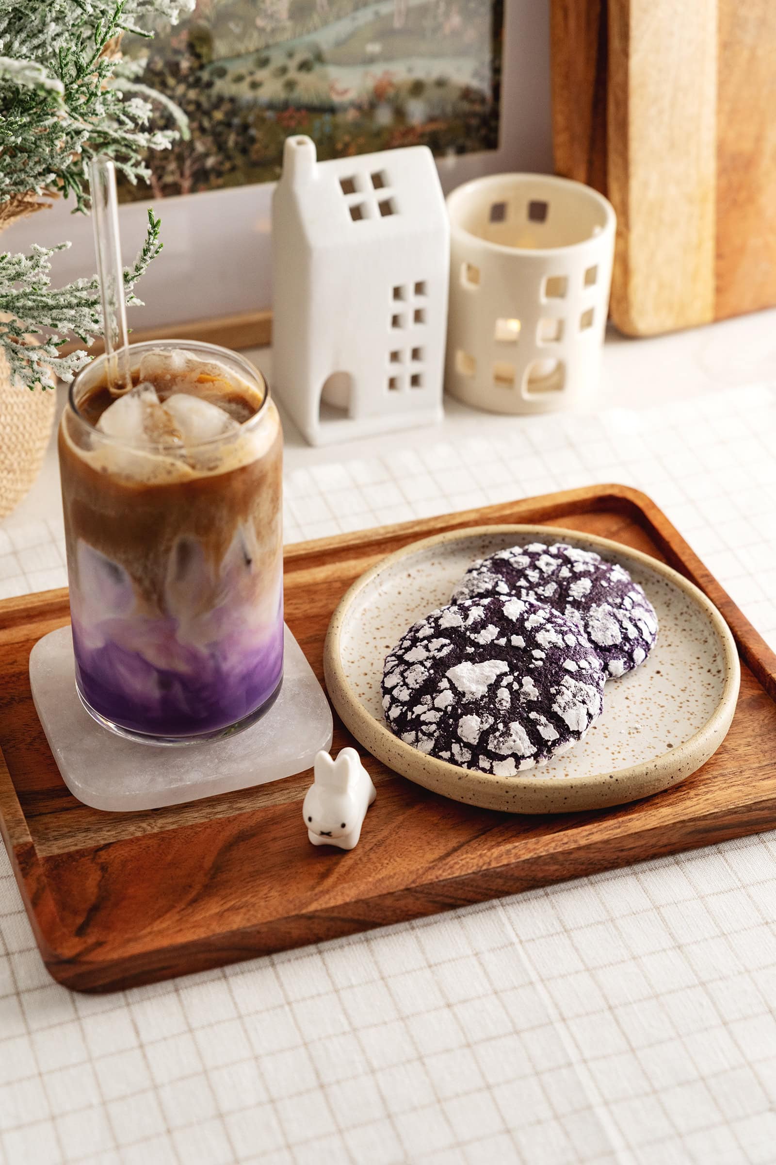Two ube crinkle cookies on a plate with a glass of ube latte on a wooden tray.